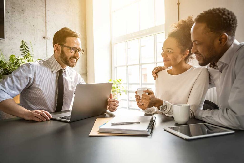 Parent reviews household finances with a partner at a kitchen table beside bills and a calculator.