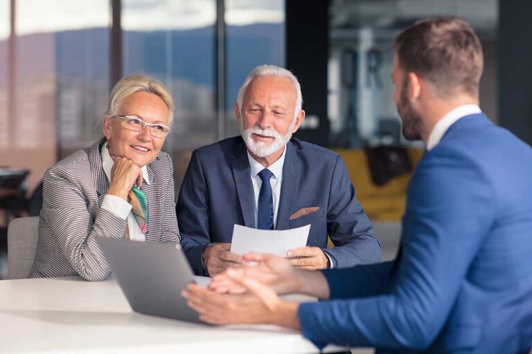A young family and an older couple reviewing insurance documents together at a kitchen table.